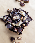 Dark chocolate brittle topped with crushed pecans and sea salt, broken into pieces on parchment paper.