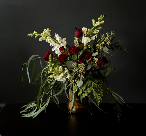 Bouquet of red and white flowers with greenery in a vase against a black background