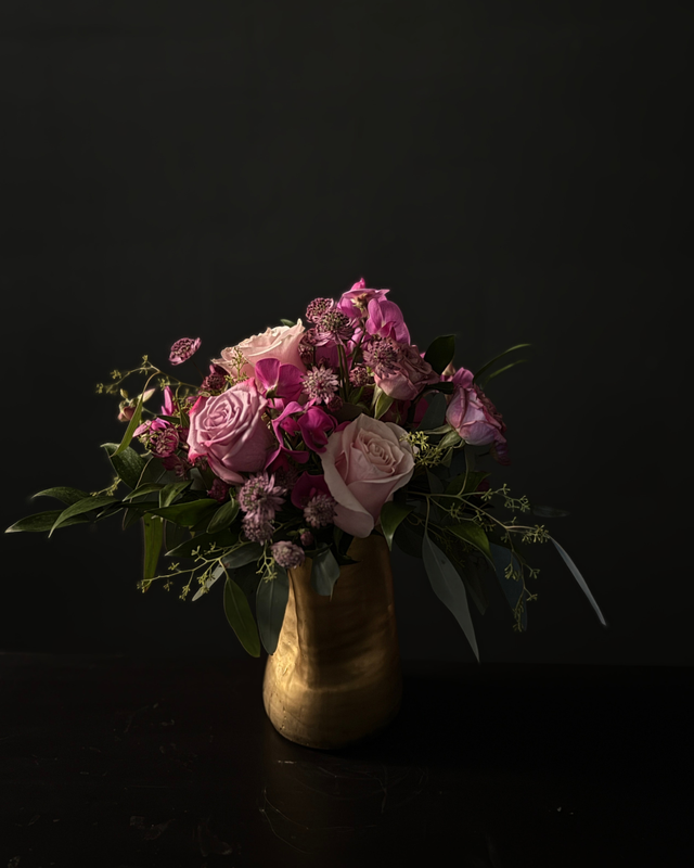 Bouquet of pink and purple flowers in a gold vase on a dark background