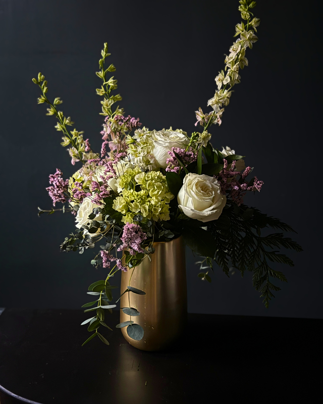 Floral arrangement in a gold vase against a dark background